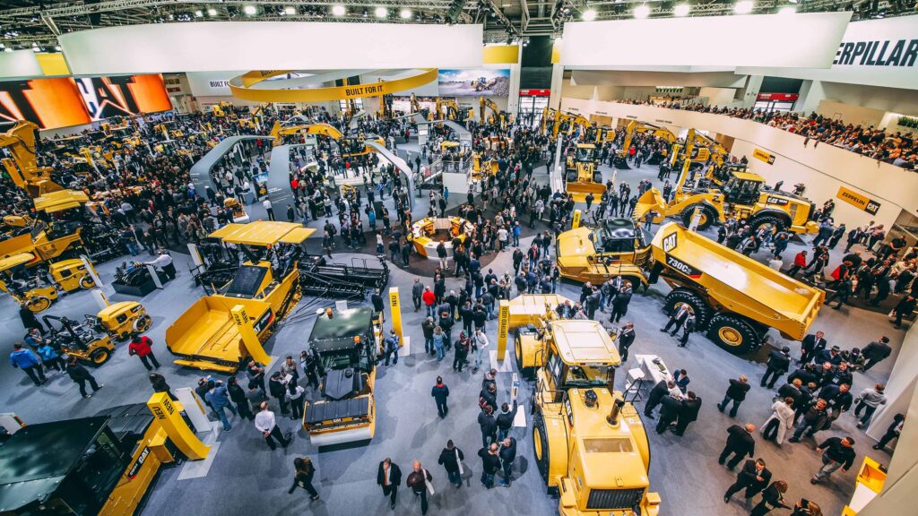Bauma. Messehalle. Auf dem Bild sind verschiedene Baumaschinen und Messebesucher zu sehen.